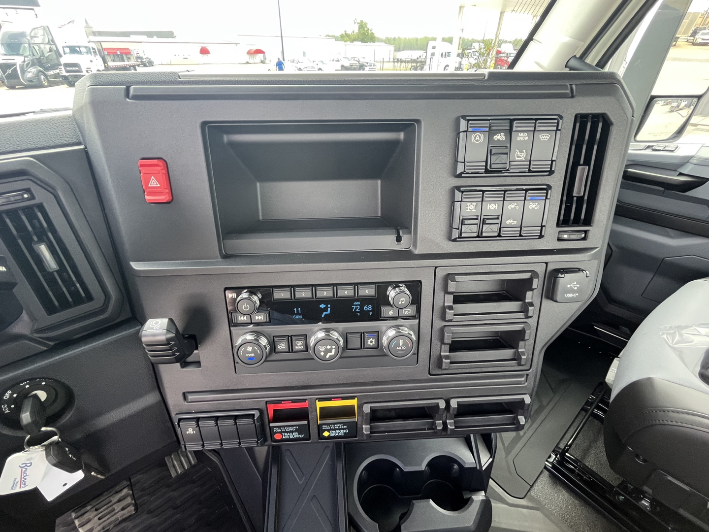 Truck cab dashboard featuring control panel with climate knobs, dual cup holders, and assorted switches in view.