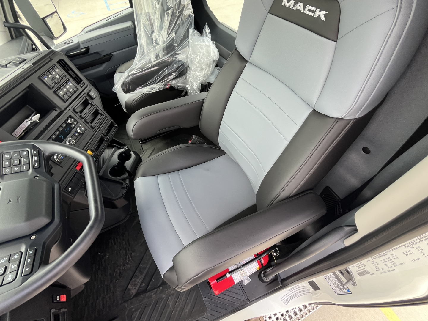 Truck cab interior showing steering wheel, dashboard, and gray/black seats with Mack logo on headrest.