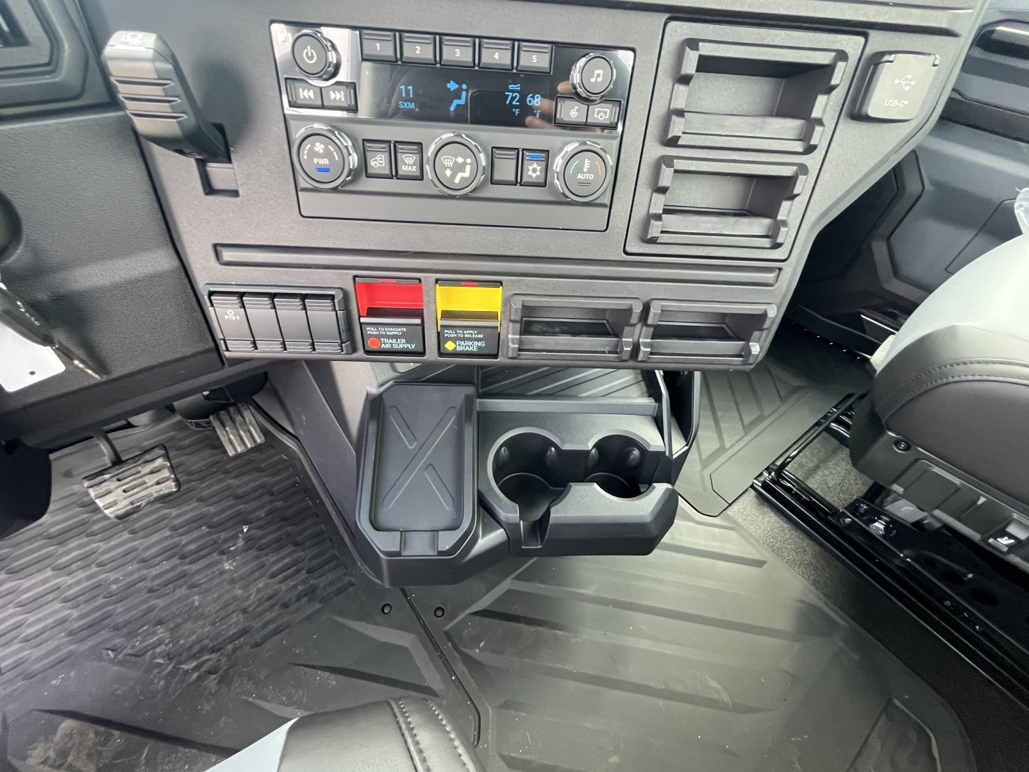 Cab interior of a 2027 Mack AN64T showing dashboard controls, climate controls, cup holders, and a storage tray.