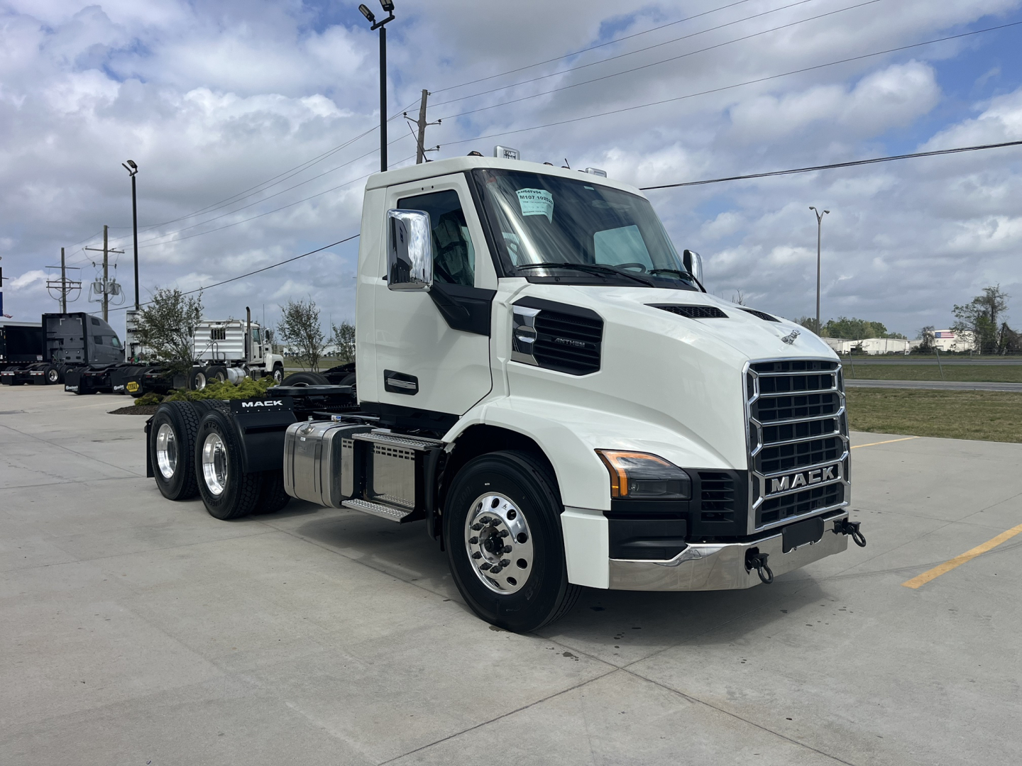 Truck cab with Mack AN64T badge in front, white exterior, large grille, dual rear axles, side mirrors, fuel tank, and chassis on a lot.