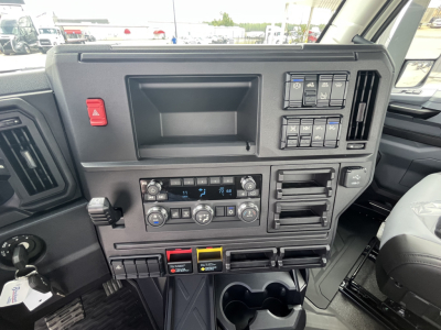 Truck cab dashboard featuring control panel with climate knobs, dual cup holders, and assorted switches in view.