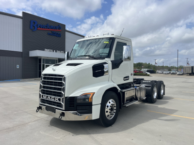 Mack AN64T conventional daycab truck in front of dealership building, white cab, triple-axle rear, prominent grille, Mack emblem, side mirrors, chrome bumper