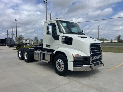 Truck cab with Mack AN64T badge in front, white exterior, large grille, dual rear axles, side mirrors, fuel tank, and chassis on a lot.