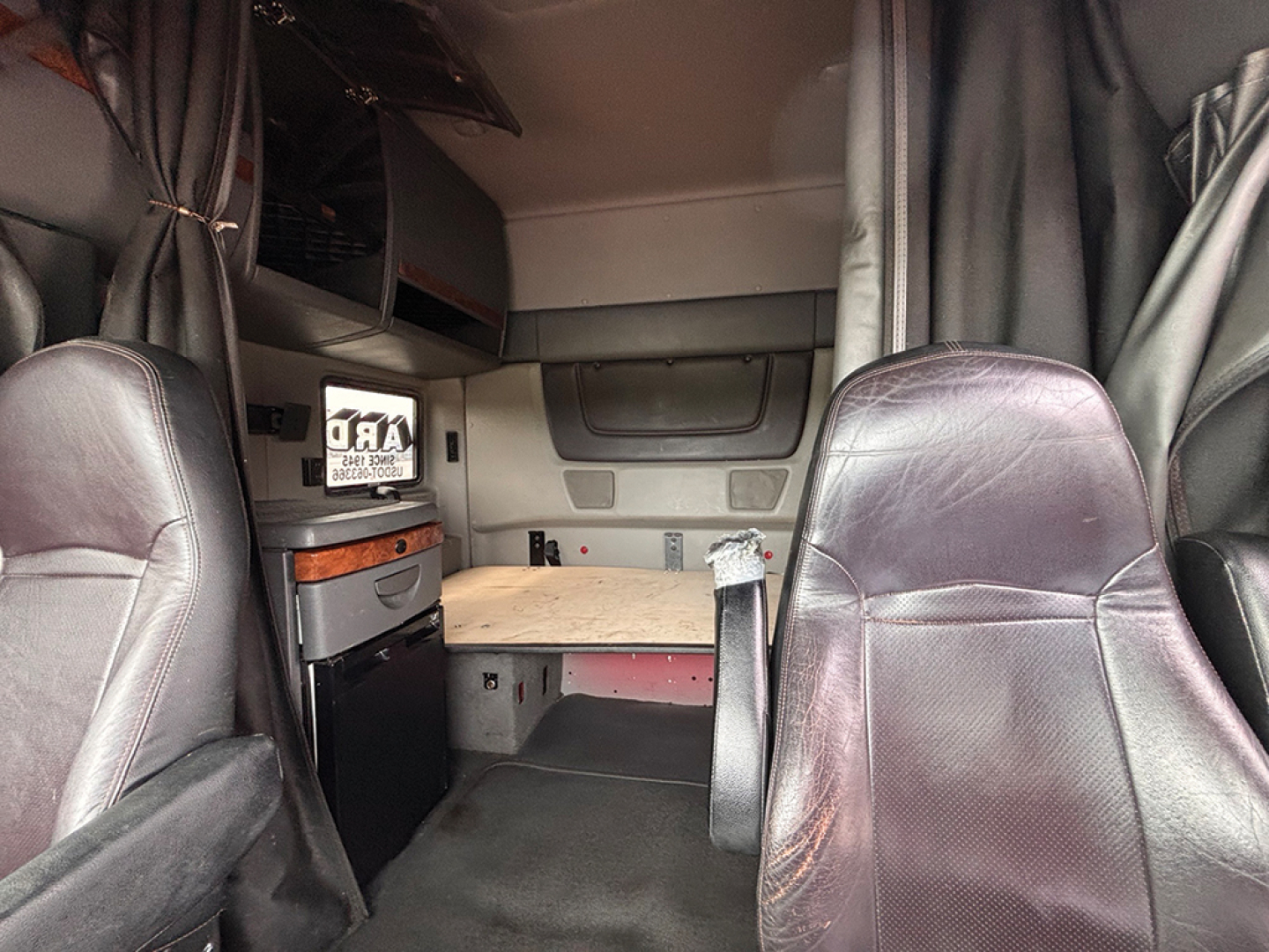 Interior cab view of a 2020 International LT625 sleeper. Visible features include a sleeper bed area, overhead cabinets, wood desk surface, and leather seats.