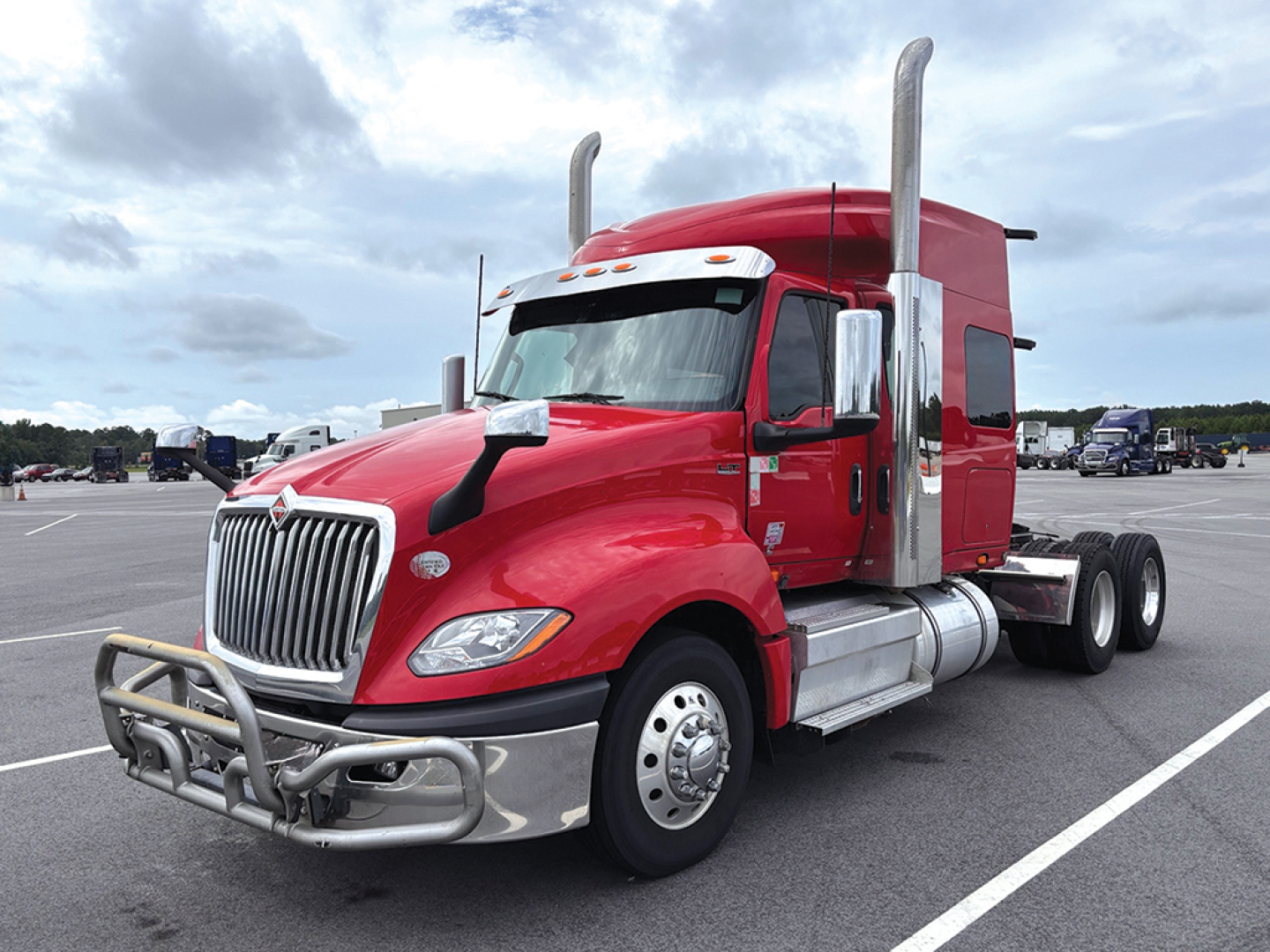 Truck cab with red International LT625 sleeper, chrome front bumper guard, dual vertical exhaust stacks, large grille, side fuel tanks, in-service condition.