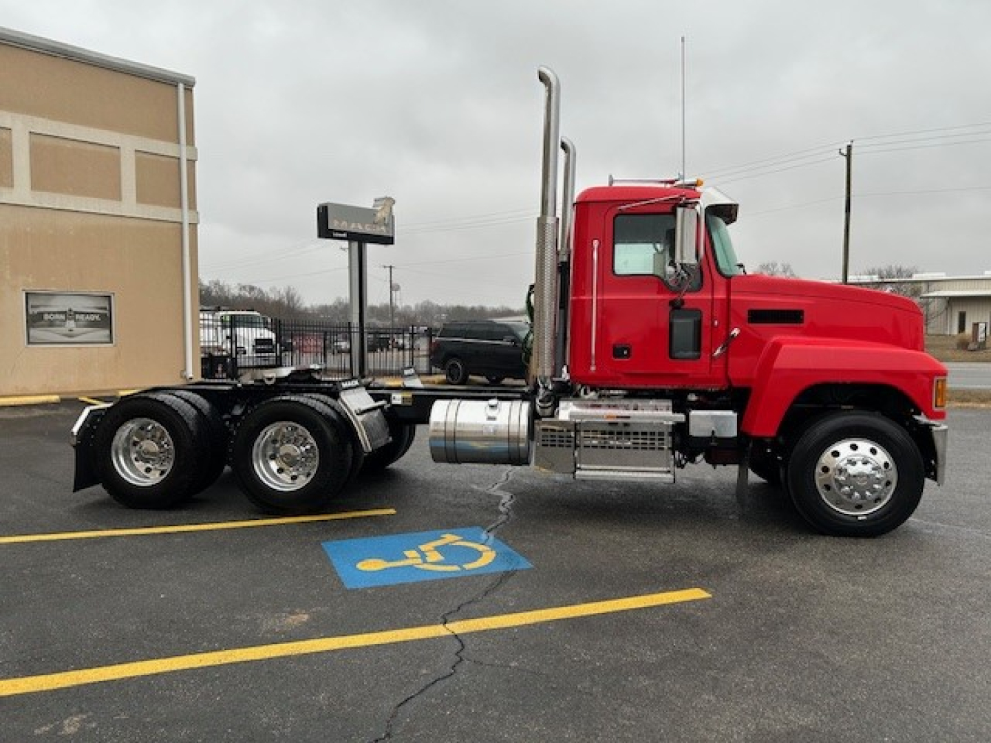 Truck cab and chassis: red 2026 Mack PI64T daycab with dual rear axles on a dealership lot.