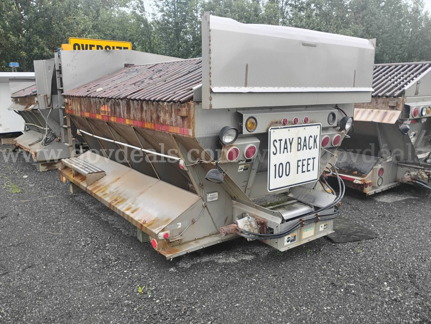 Dump truck trailer showing rear with tailgate and lights, Stay Back 100 Feet sign, rust-free metal components, and dump bed in view.