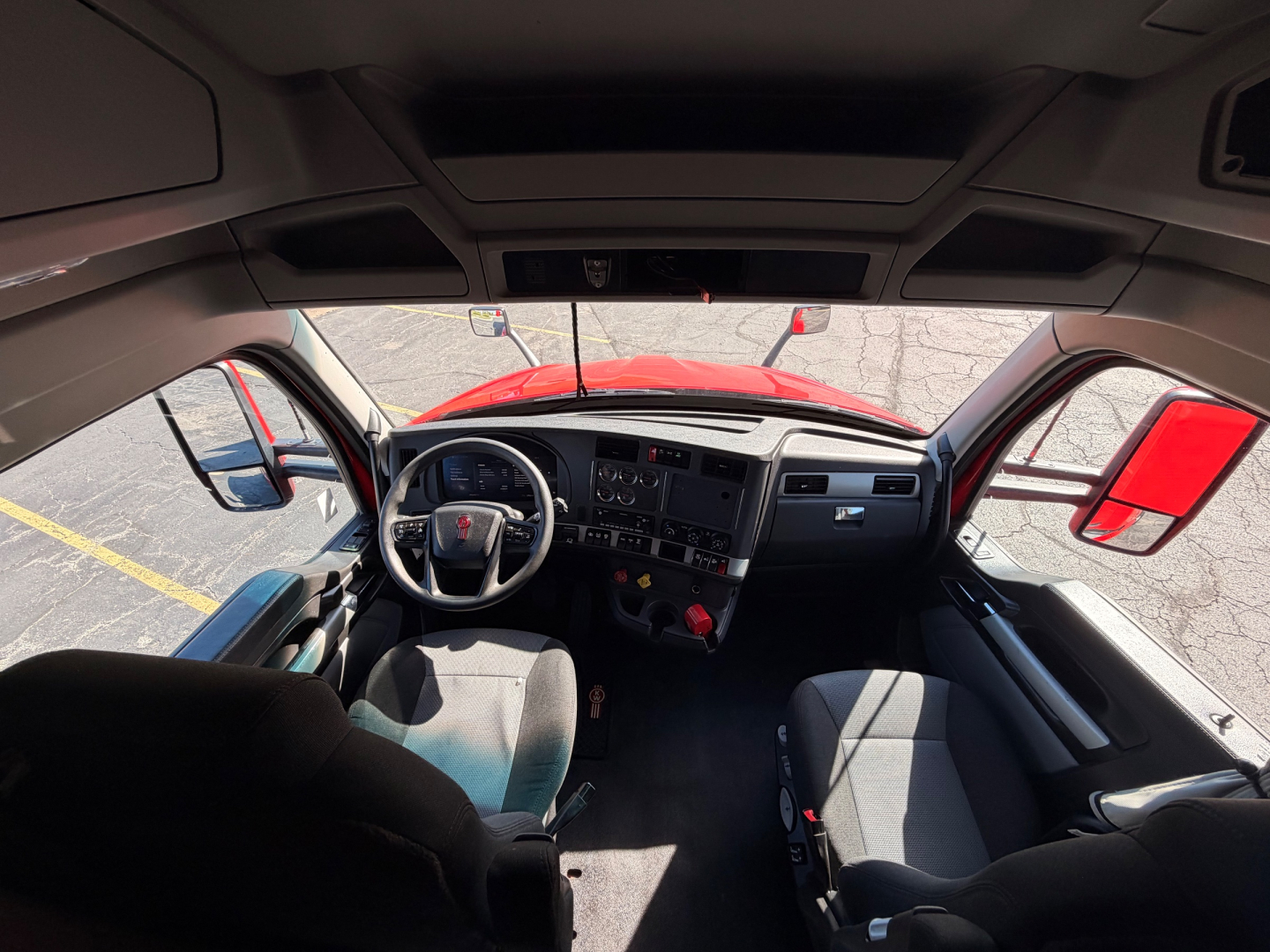 Kenworth cab interior of a 2023 T680 viewed from the passenger seat, with steering wheel, dashboard, and front seats visible.