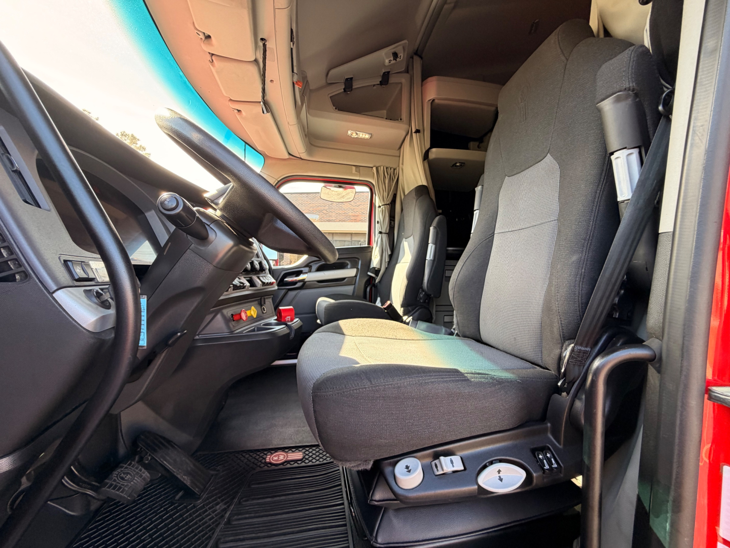 Kenworth T680 cab interior view from open door showing driver's seat and dashboard with steering wheel and controls.