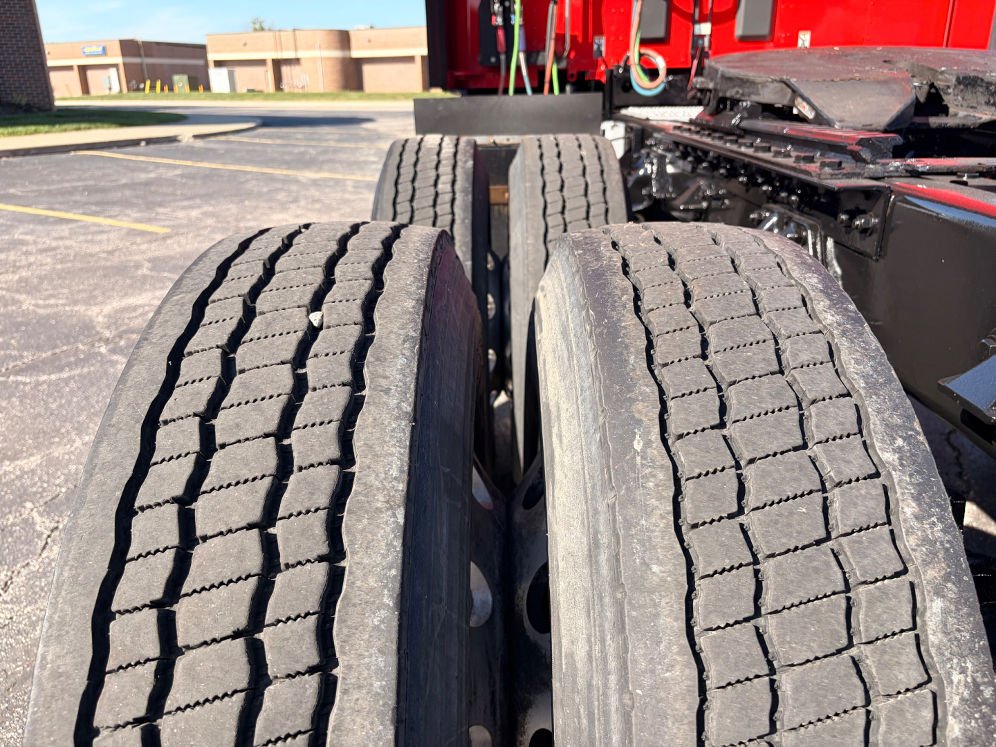 Dual rear truck tires on a Kenworth T680 chassis showing tread patterns and dual wheel setup with red cab visible in background.