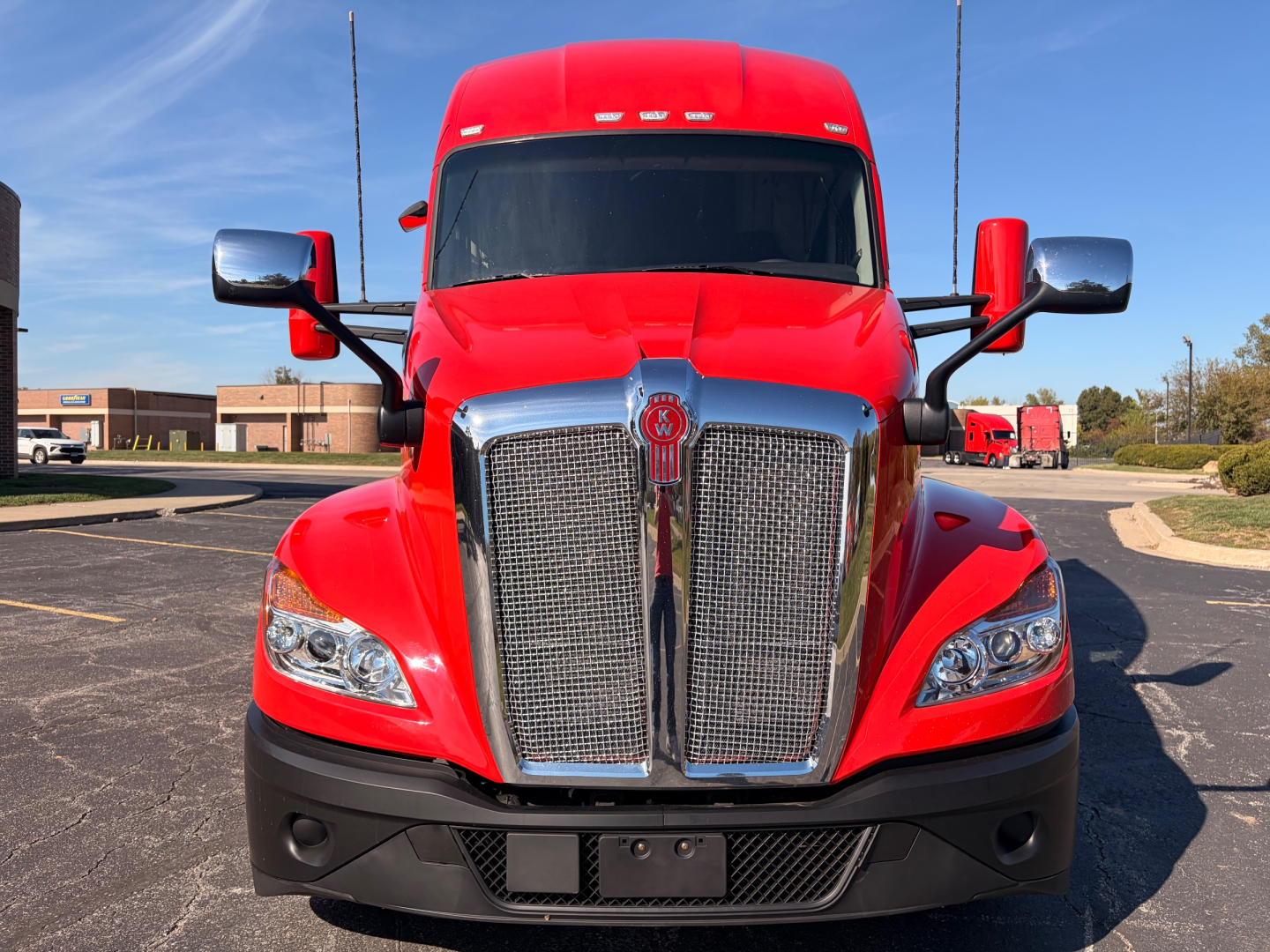 Kenworth T680 front view showing chrome grille and red cab with black bumper and side mirrors.