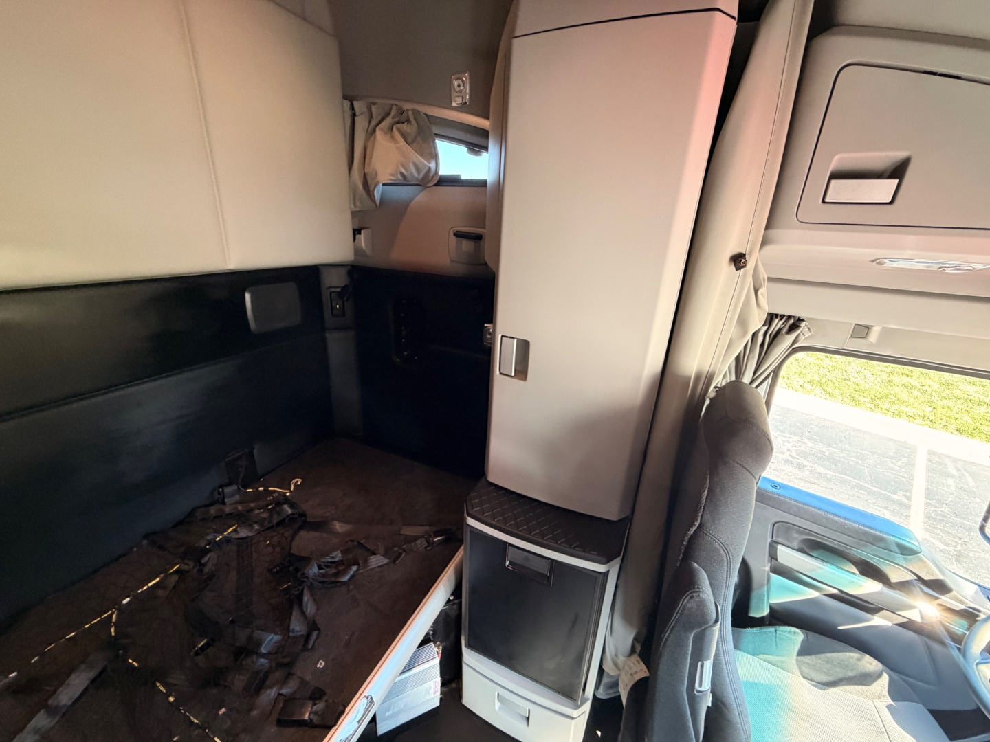 Kenworth interior sleeper cab showing dashboard and small cabinetry, with a cluttered floor and a passenger seat visible.