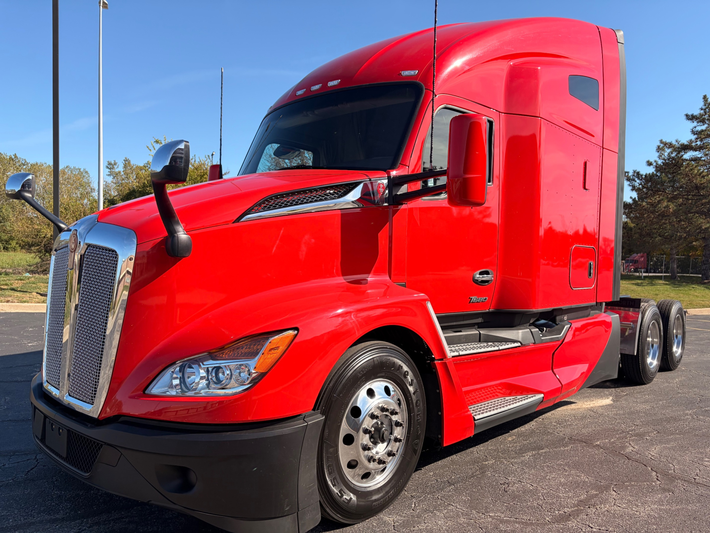 Red Kenworth T680 tractor-trailer cab side view showing aerodynamic sleeper, chrome grille, dual rear axles, and chrome steps.