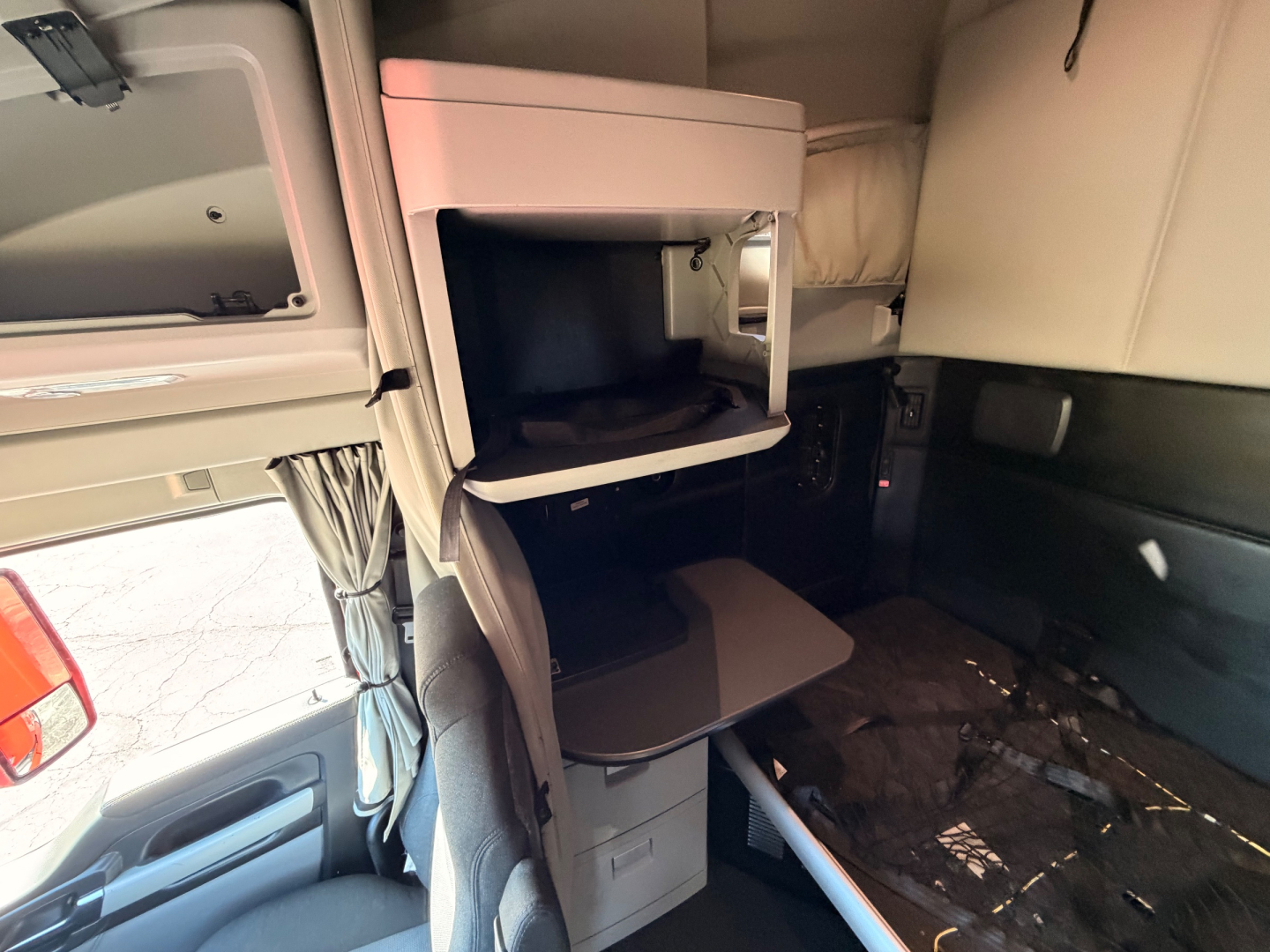Interior of a Kenworth T680 sleeper cab showing a small overhead storage compartment and a fold-outtable in the cabin area.