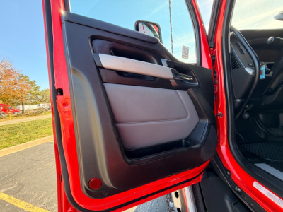 Truck door interior view of a red 2023 Kenworth T680 showing the driver's side door panel, armrest, and window controls from an open door angle.