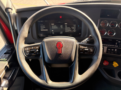 Kenworth T680 truck interior showing steering wheel with Kenworth emblem, digital dash screen, and gauge cluster with controls and warning symbols.