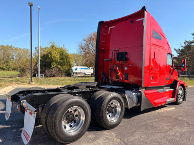 Kenworth T680 tractor rear-view showing triple rear axles, red cab, fifth wheel, and fuel tanks.