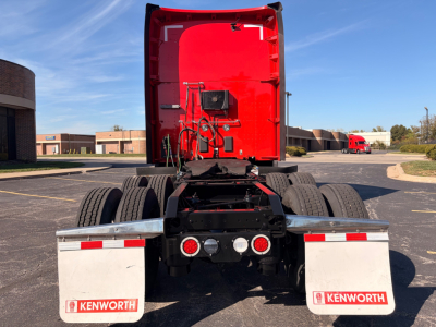 Kenworth truck rear view showing red sleeper cab and dual rear wheels, with Kenworth mud flaps and taillights.