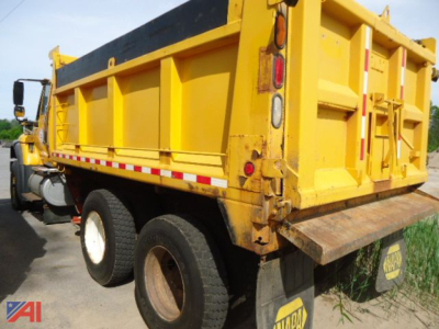 Dump truck side spreader with yellow dump body and wing, rear view showing tailgate and dual rear tires.