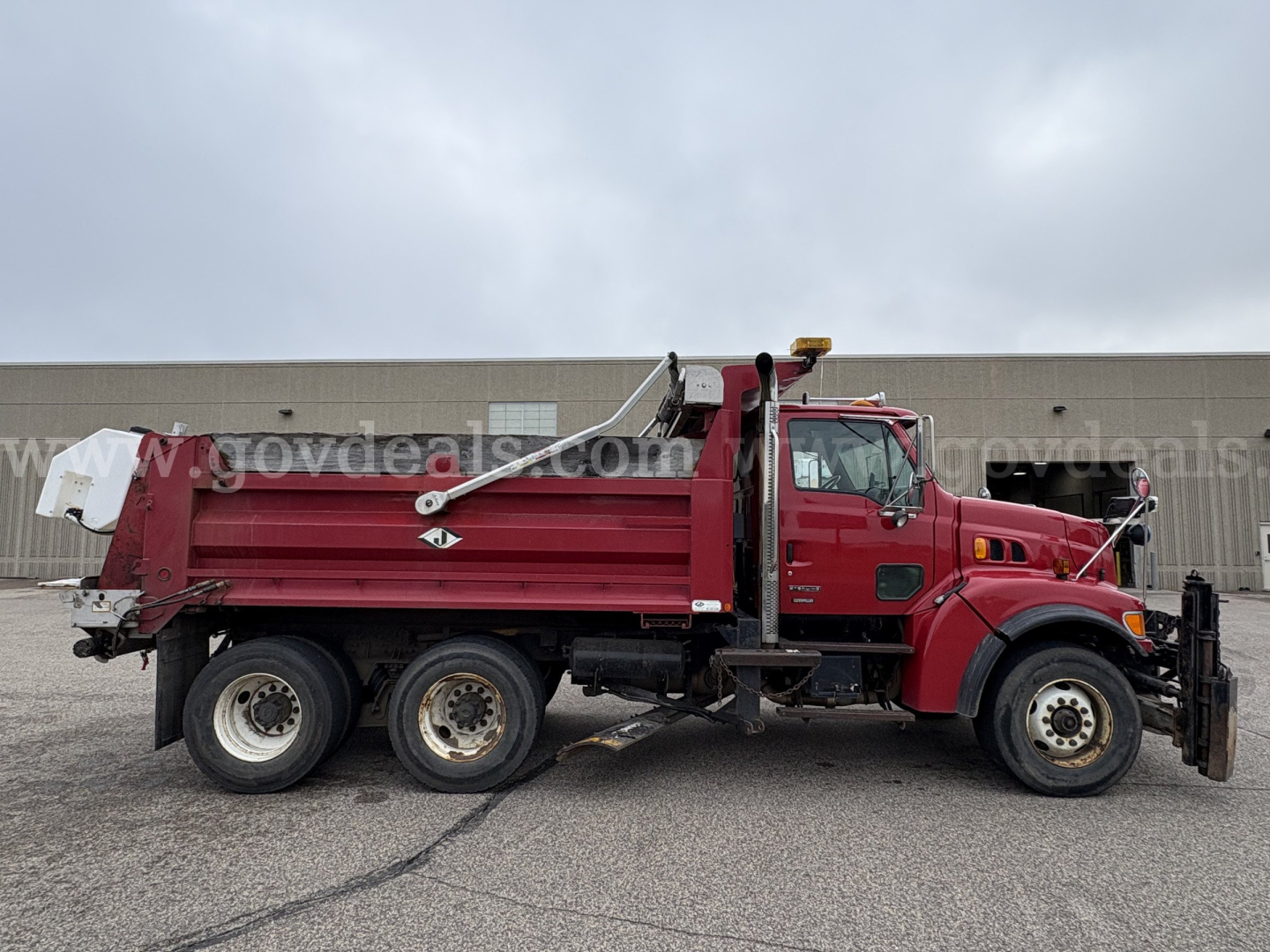 Side view of a red 2001 Sterling LT9500 dump truck with a plow, triple rear axles, and hydraulic dump bed.