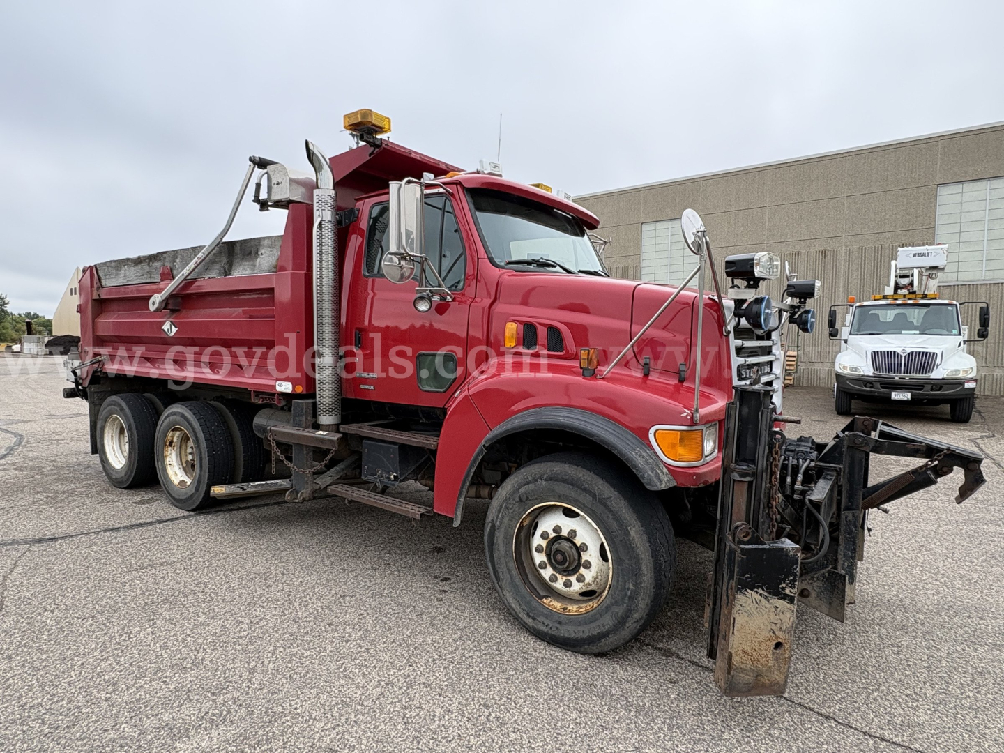 Truck side view showing red Sterling LT9500 plow truck with front snow plow attachment, dual rear wheels, and aerial lighting on cab.