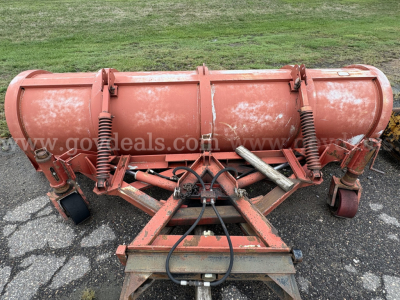 Front view of orange plow equipment with large cylindrical tank and springs, showing hydraulic hoses and hitch.