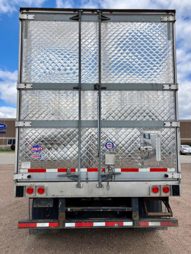 Rear view of a 2022 utility reefer trailer with diamond plate aluminum doors, hinges, and latches. Stocked with reflective red and white tape, taillights, and undercarriage visible.