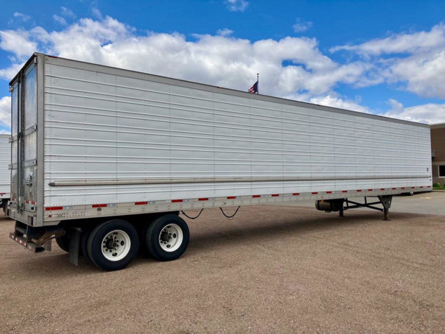 Utility reefer trailer showing tandem axles, silver corrugated side, and rear doors. No visible text on body.