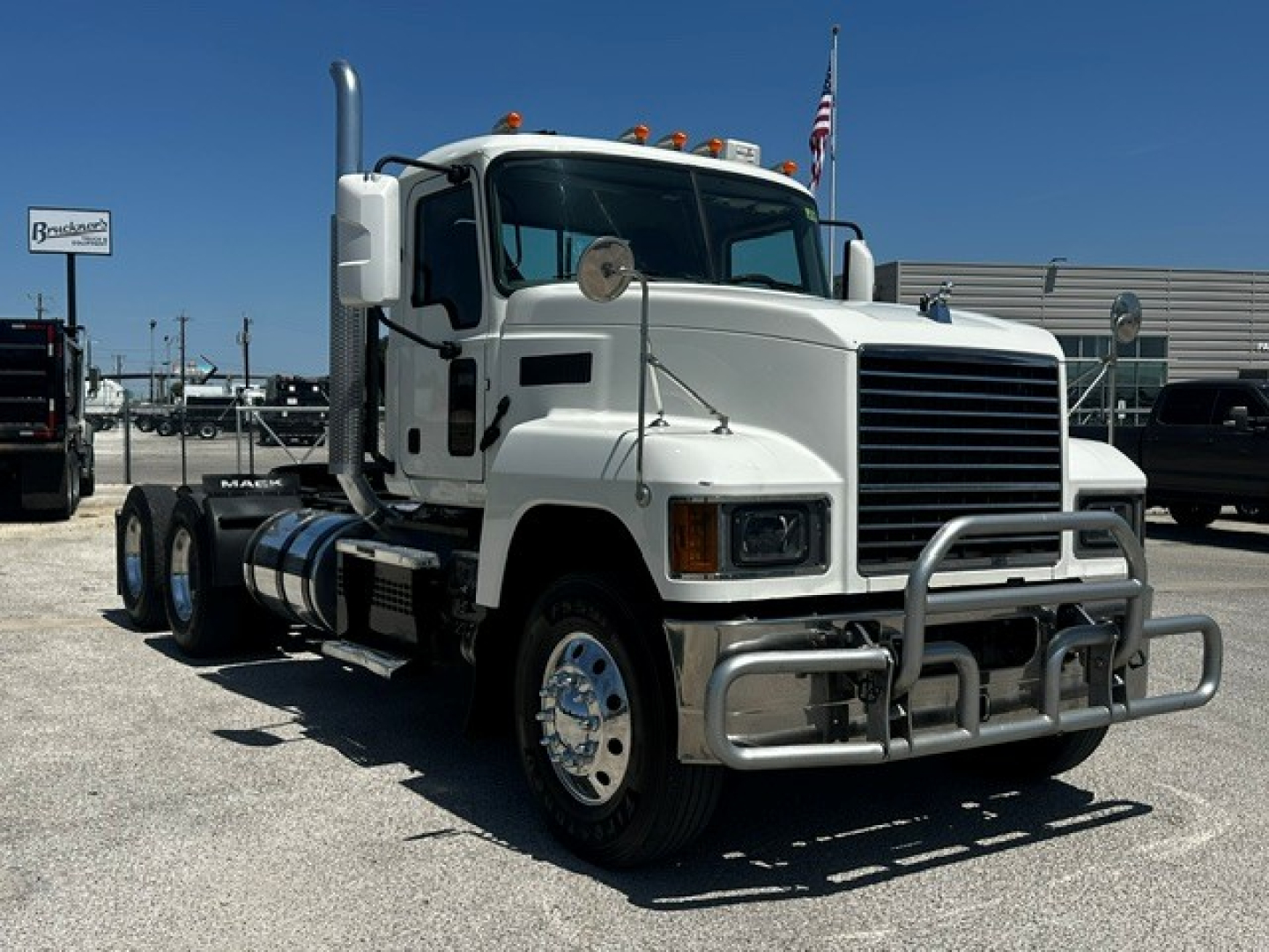 White 2020 Mack PI64T conventional daycab truck in a dealership lot, front grille with chrome bumper guard and dual exhaust stacks, stock # W0049, VIN plate not visible.