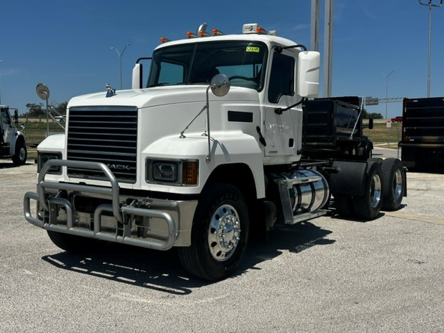 Truck cab exterior showing Mack PI64T chassis, front grille, bumper guard, and dual rear axles with fifth wheel in a parking lot.