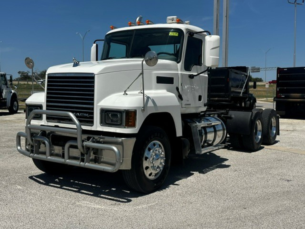 Truck cab exterior showing Mack PI64T chassis, front grille, bumper guard, and dual rear axles with fifth wheel in a parking lot.