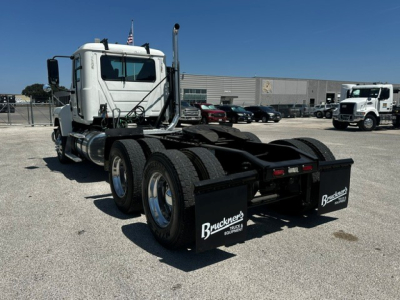 Mack PI64T truck tractor with dual rear axle and chassis showing Brackett's mud flaps and rear tires; white cab, fuel tanks, and equipment in background.