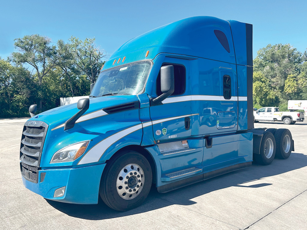 Truck image: blue 2021 Freightliner Cascadia126 sleeper cab, side view with chrome grille, dual rear axles, Freightliner branding.