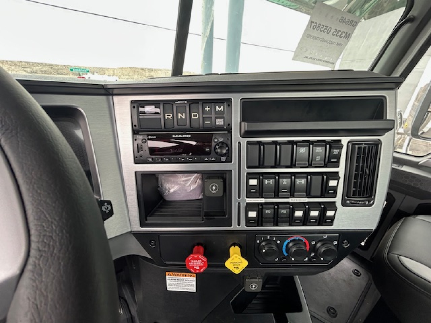 Dashboard cockpit of a 2026 Mack GR64B truck showing control panel, switches, climate controls, and steering wheel; no visible text besides dashboard controls.