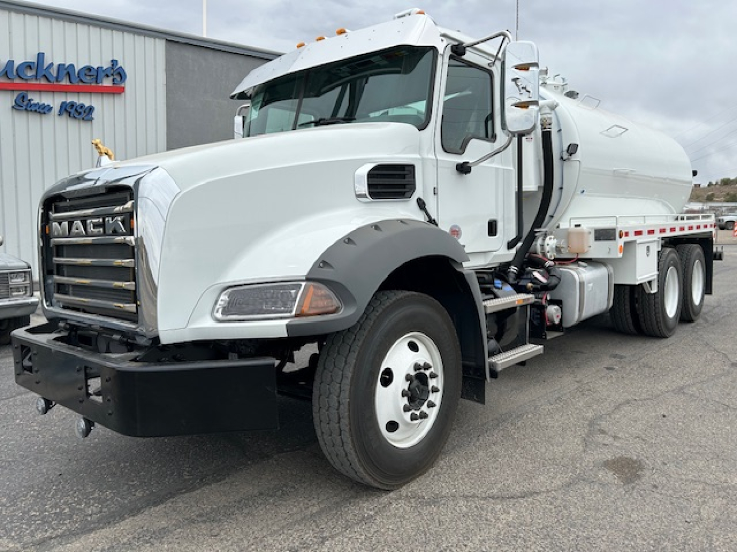 Mack GR64B vacuum tank truck with white cab and large front grille, side view showing tank and dual rear axles.