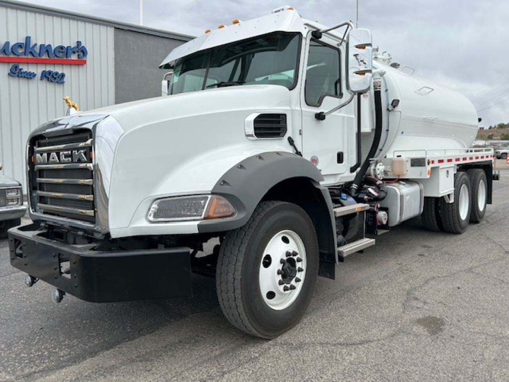 Mack GR64B vacuum tank truck with white cab and large front grille, side view showing tank and dual rear axles.