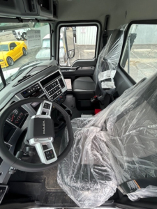 Cab interior of 2026 Mack GR64B vacuum tanker showing steering wheel, dashboard with controls, and plastic-wrapped driver seat.