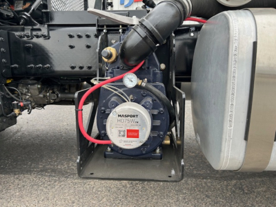 Mack GR64B vacuum tank truck side showing auxiliary pump with gauge and red hose connected, fuel/air lines and metal frame.