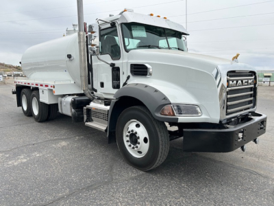 Mack GR64B vacuum tank truck side view showing front grille with Mack emblem, large fuel/air intake, side step, and white cylindrical vacuum tank behind cab.
