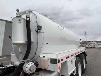 Mack GR64B vacuum tank truck in side view showing white cylindrical tank with hoses and controls on rear