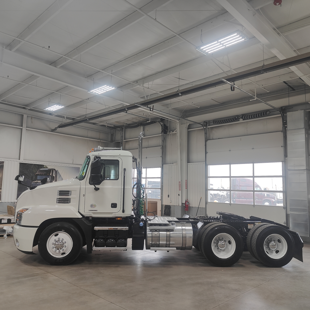 Truck side profile showing 2020 Mack AN64T conventional daycab with fuel tanks and dual rear axles inside a showroom.
