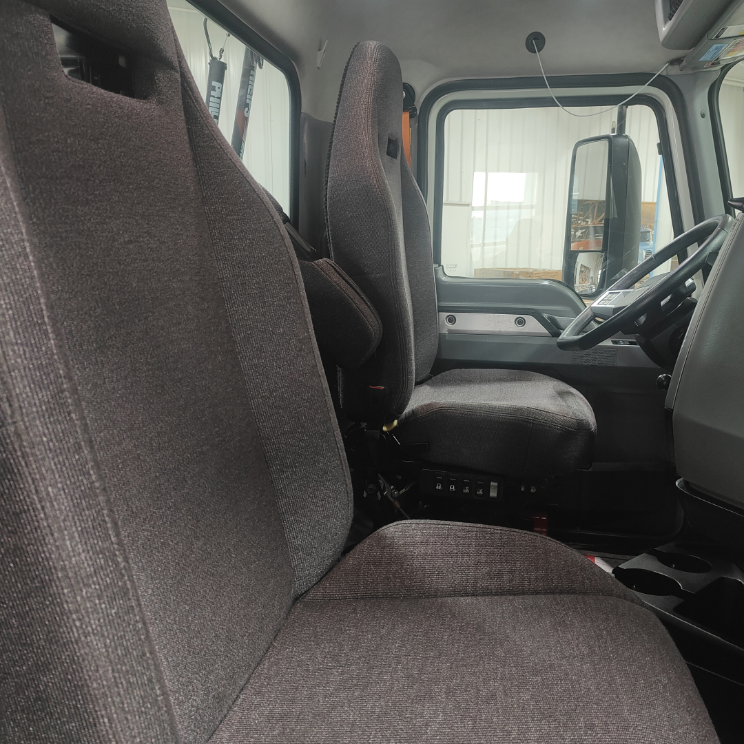 Truck cab interior showing driver seat and passenger seat with gray fabric, dashboard, steering wheel, and door panels in view.