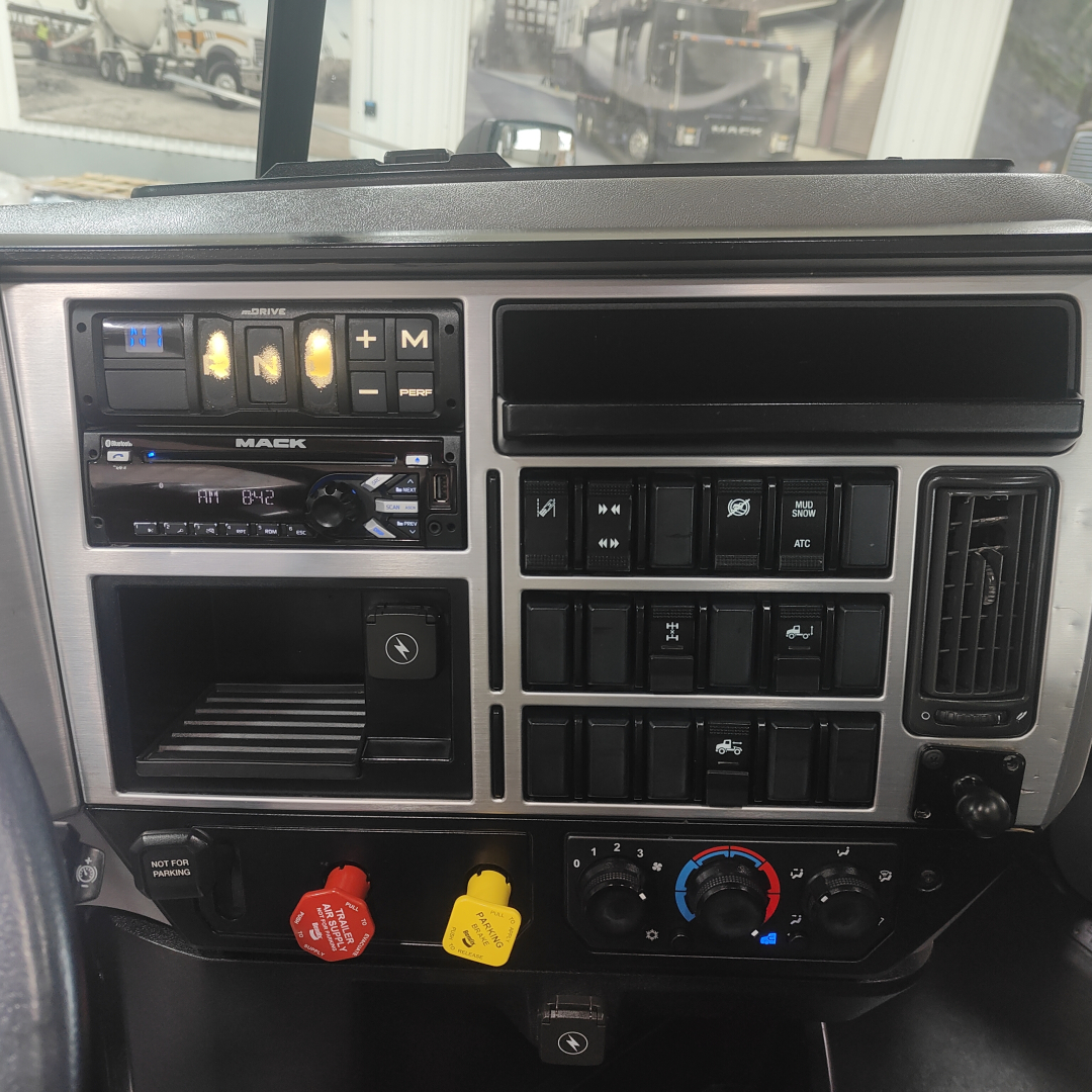 Dashboard of a 2020 Mack AN64T showing instrument cluster, radio, climate controls, and various switches.