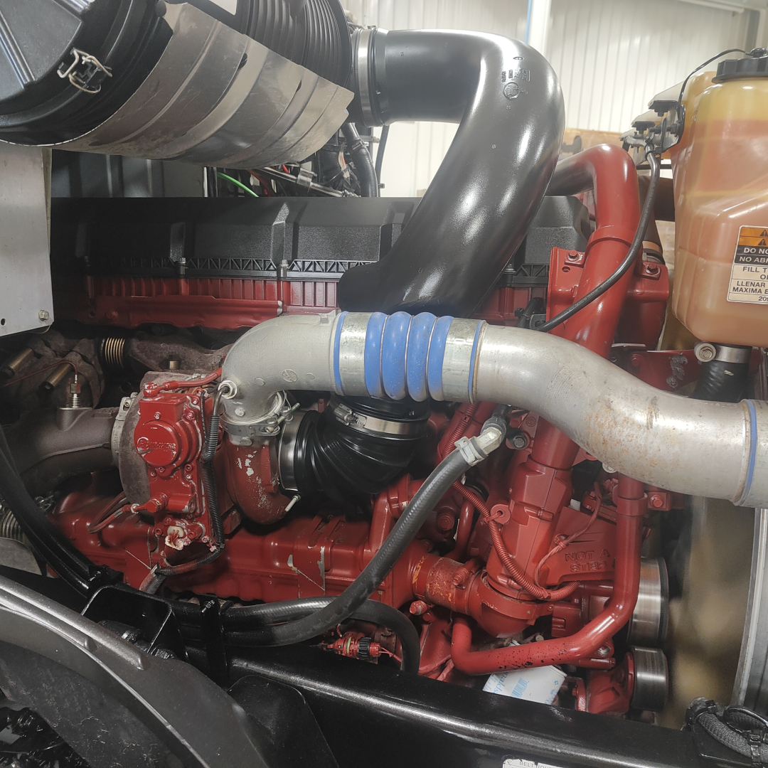Mack AN64T engine bay showing air intake hose, coolant reservoir, and red engine components.