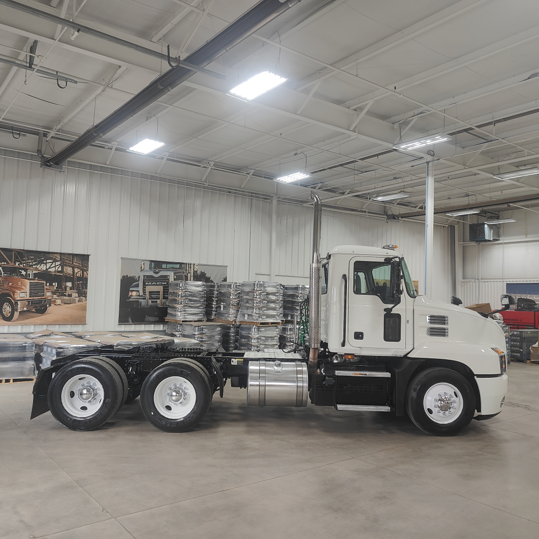Truck chassis cab in a showroom with white cab and attached frame; no visible text noted on components.