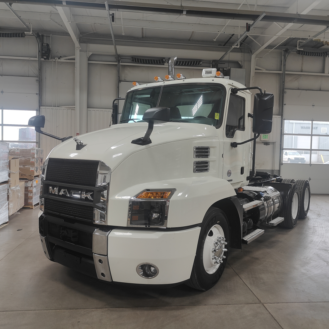 Mack AN64T conventional daycab truck in white, front-left view inside showroom, with cab and front grille readable.