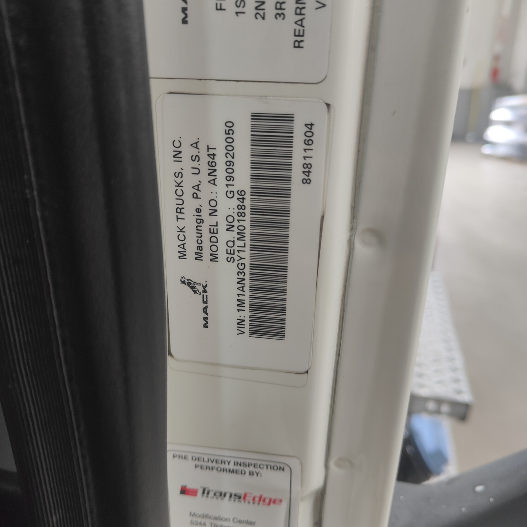 Label on Mack truck door showing VIN and model data for 2020 AN64T with barcode, MAC Trucks Inc. and model AN64T along with serial/barcode details.