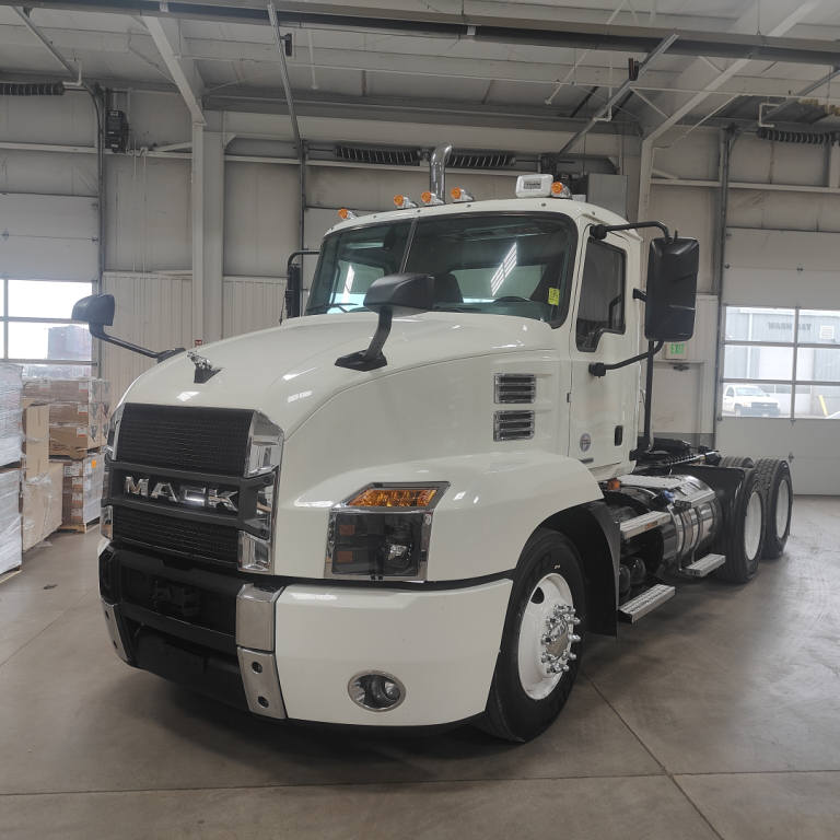 Mack AN64T conventional daycab truck in white, front-left view inside showroom, with cab and front grille readable.