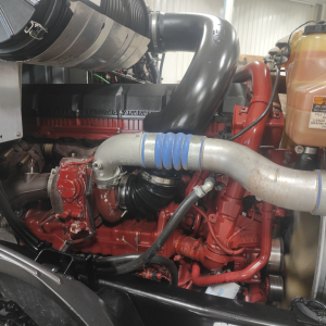 Mack AN64T engine bay showing air intake hose, coolant reservoir, and red engine components.