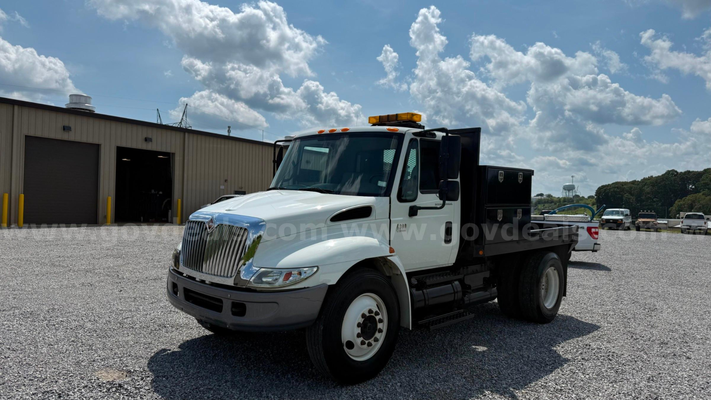 International 4300 flatbed truck in service showing front grille, cab, and flatbed bed with amber beacon light on roof.